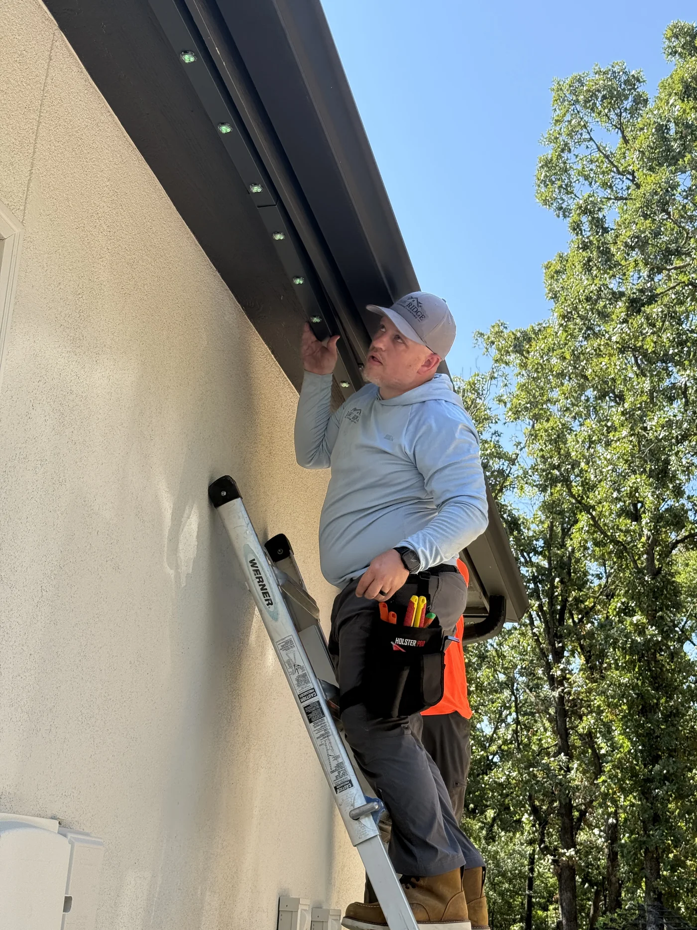 Brandon Treat installing permanent lighting track beneath a roofline